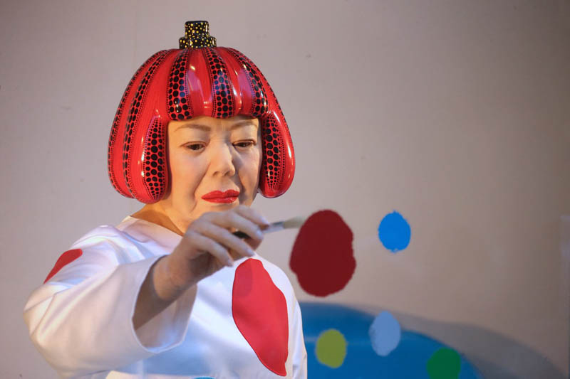 A lifelike robot of Yayoi Kusama paints spots on the window of the